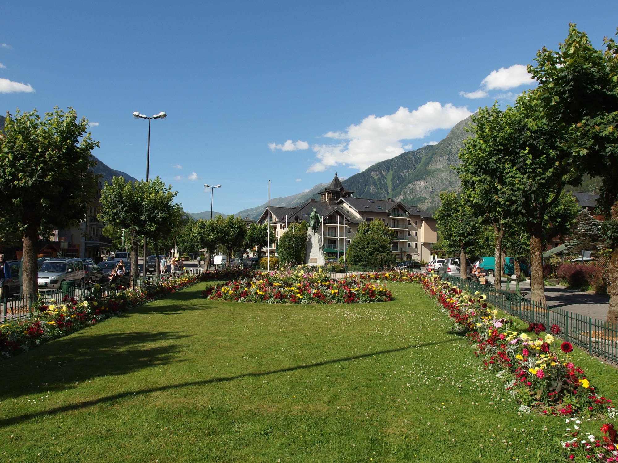Pelouse et massifs fleuris au centre de Chamonix-Mont-Blanc un après-midi de juillet, chalets et versant boisé de la montagne en arrière-plan