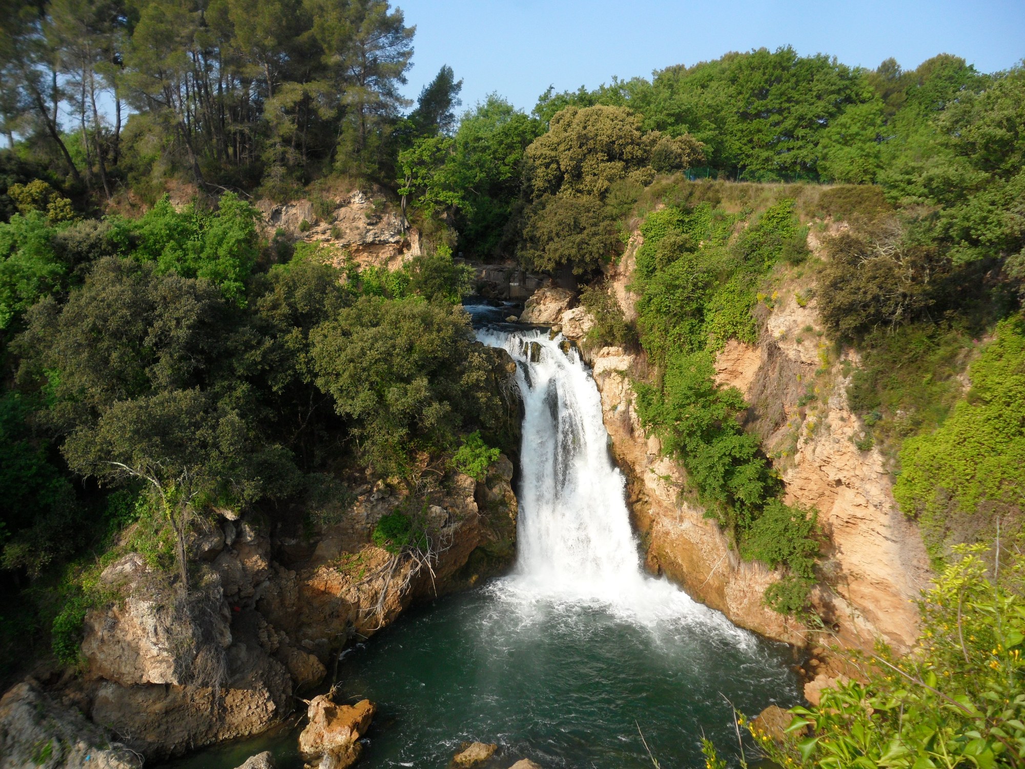 La cascade du saut du Capelan à La Motte : la Nartuby tombe dans une vasque verte entre des falaises ocre, chênes verts et pins sur les deux rives